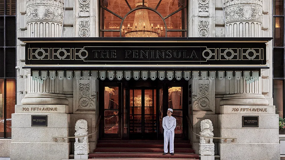 The Peninsula New York entrance on Fifth Avenue with ornate stonework and a hotel page